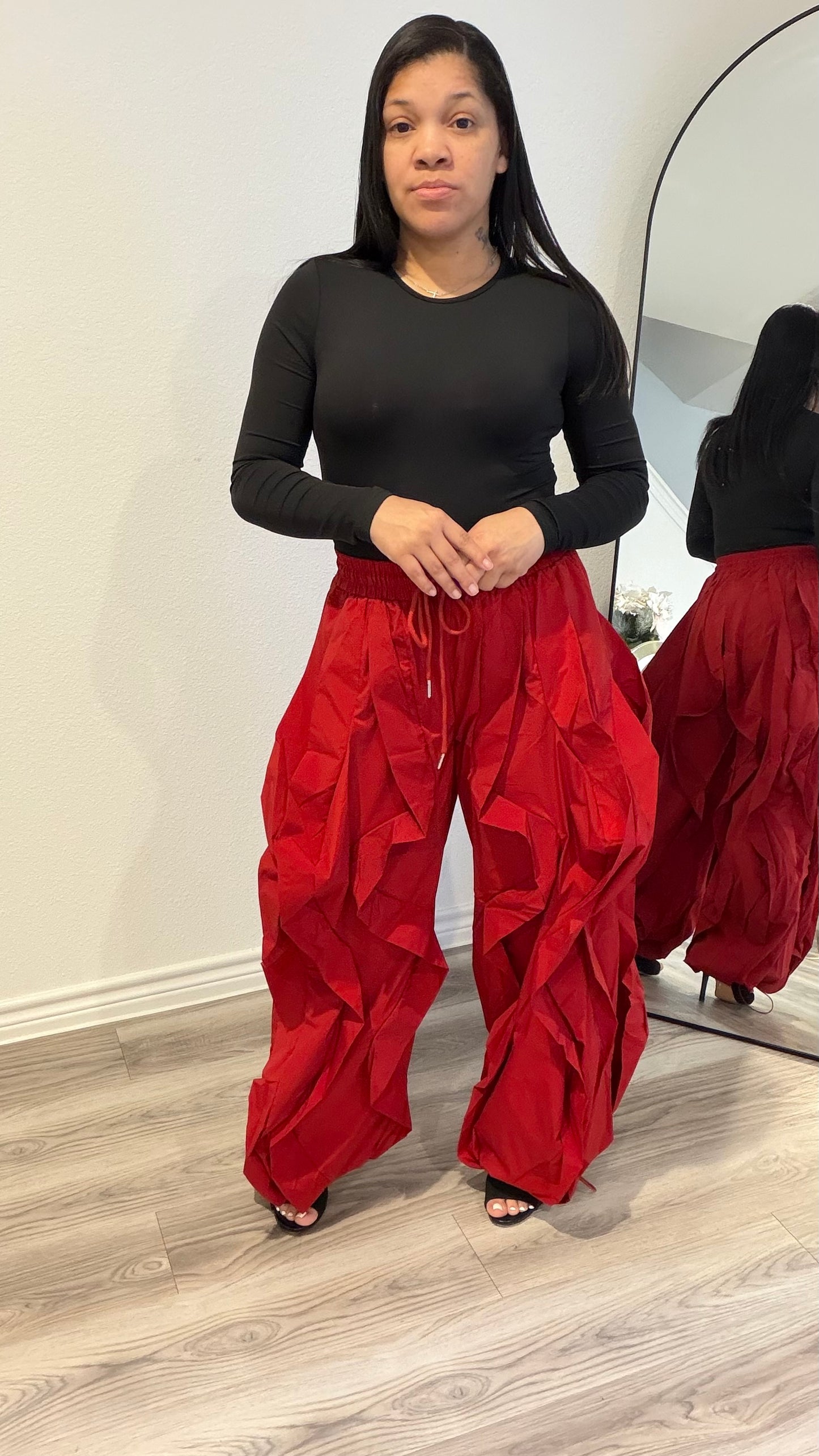 Woman wearing a fitted black long sleeve bodysuit with a smooth, second-skin silhouette paired with red statement pants.