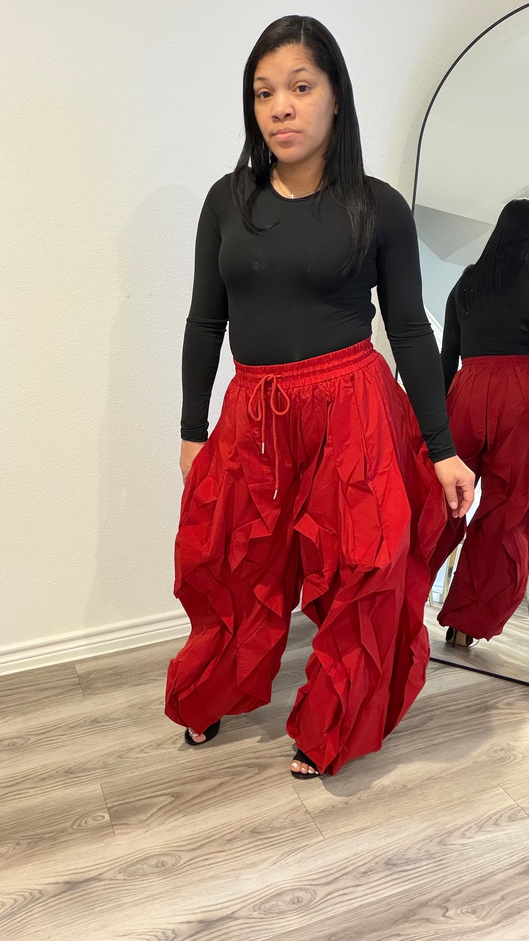 Woman wearing a fitted black long sleeve bodysuit with a smooth, second-skin silhouette paired with red statement pants.