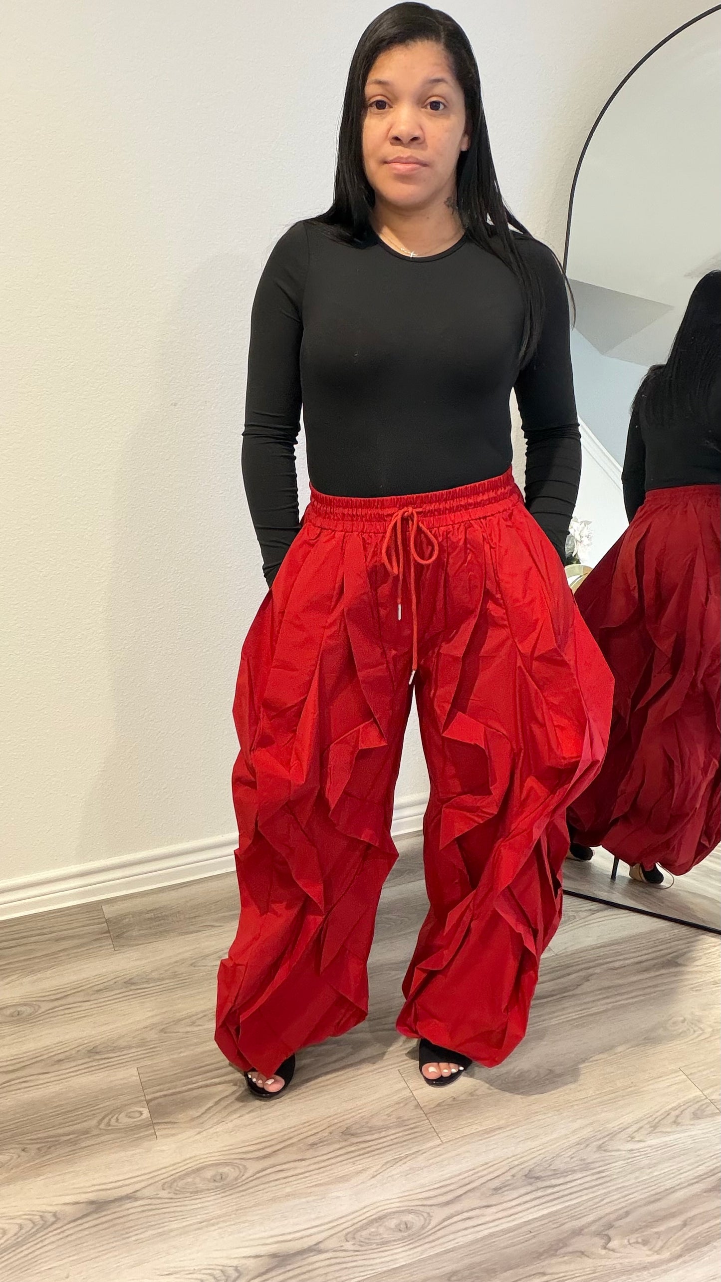 Woman wearing a fitted black long sleeve bodysuit with a smooth, second-skin silhouette paired with red statement pants.