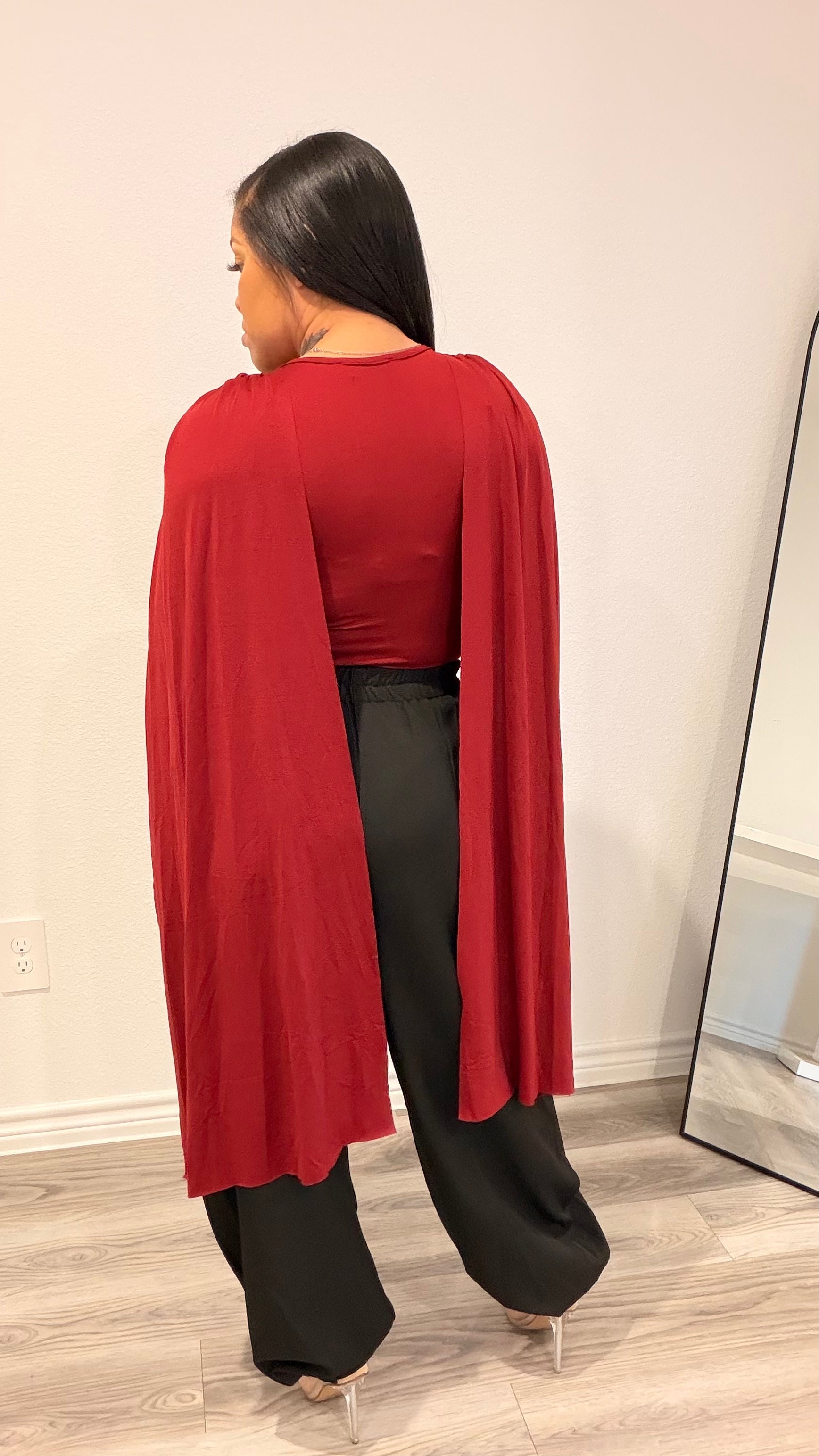 Woman wearing a bodysuit with cape-style draped sleeves and a fitted base.