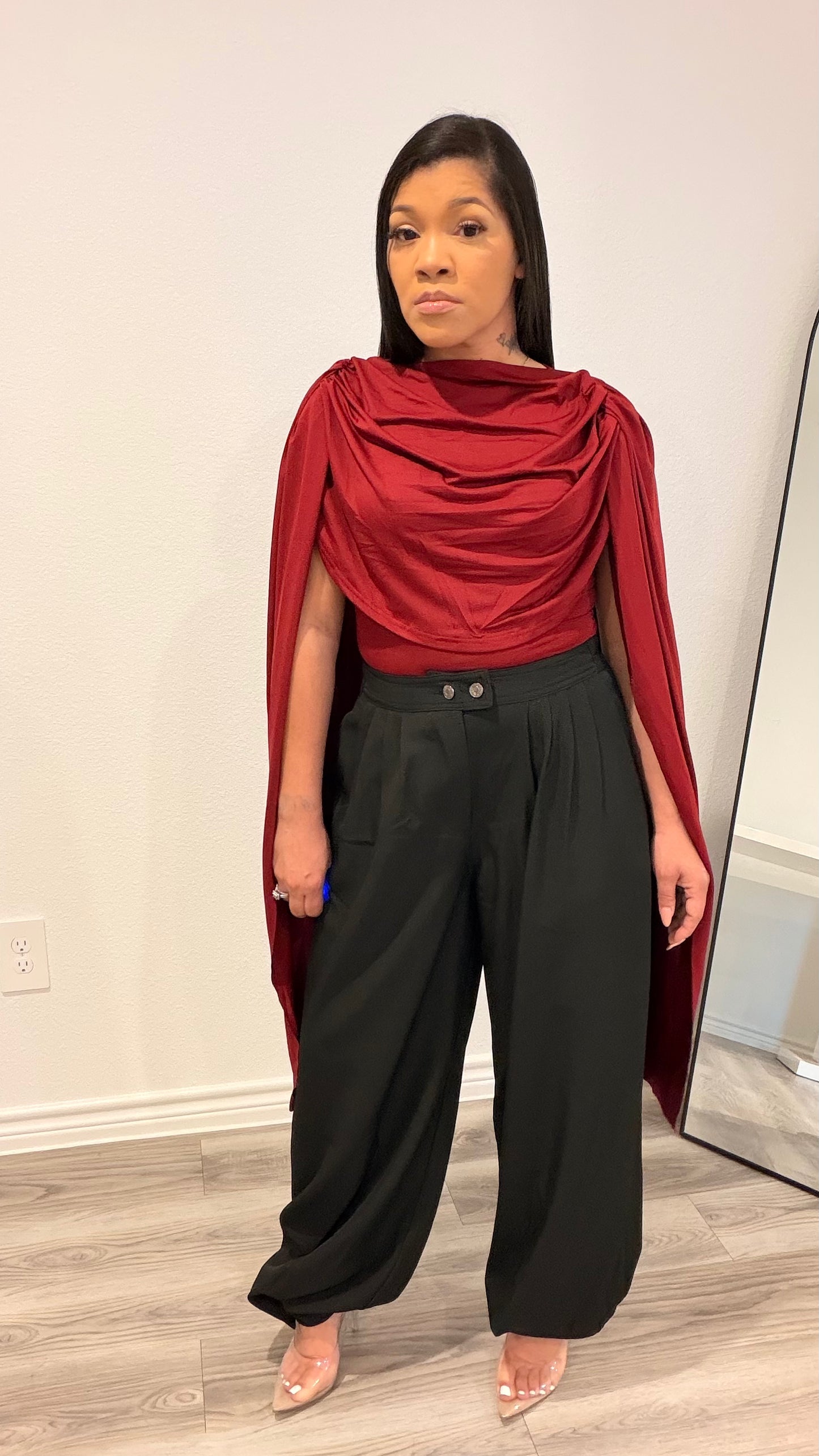 Woman wearing a bodysuit with cape-style draped sleeves and a fitted base.