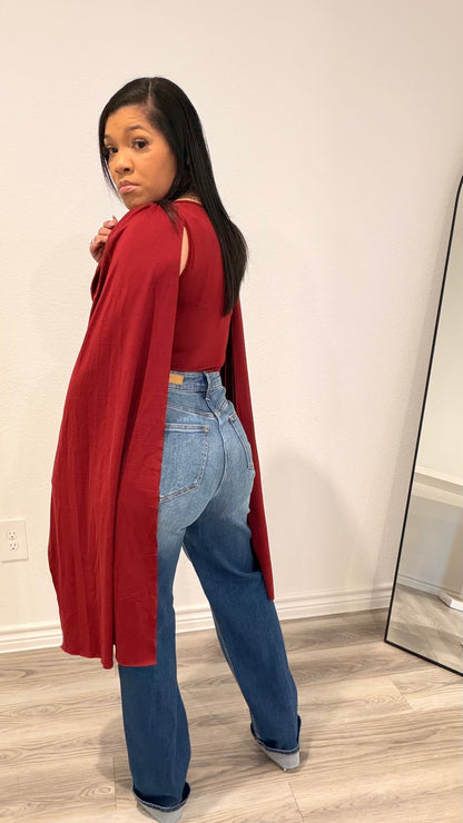 Woman wearing a bodysuit with cape-style draped sleeves and a fitted base.
