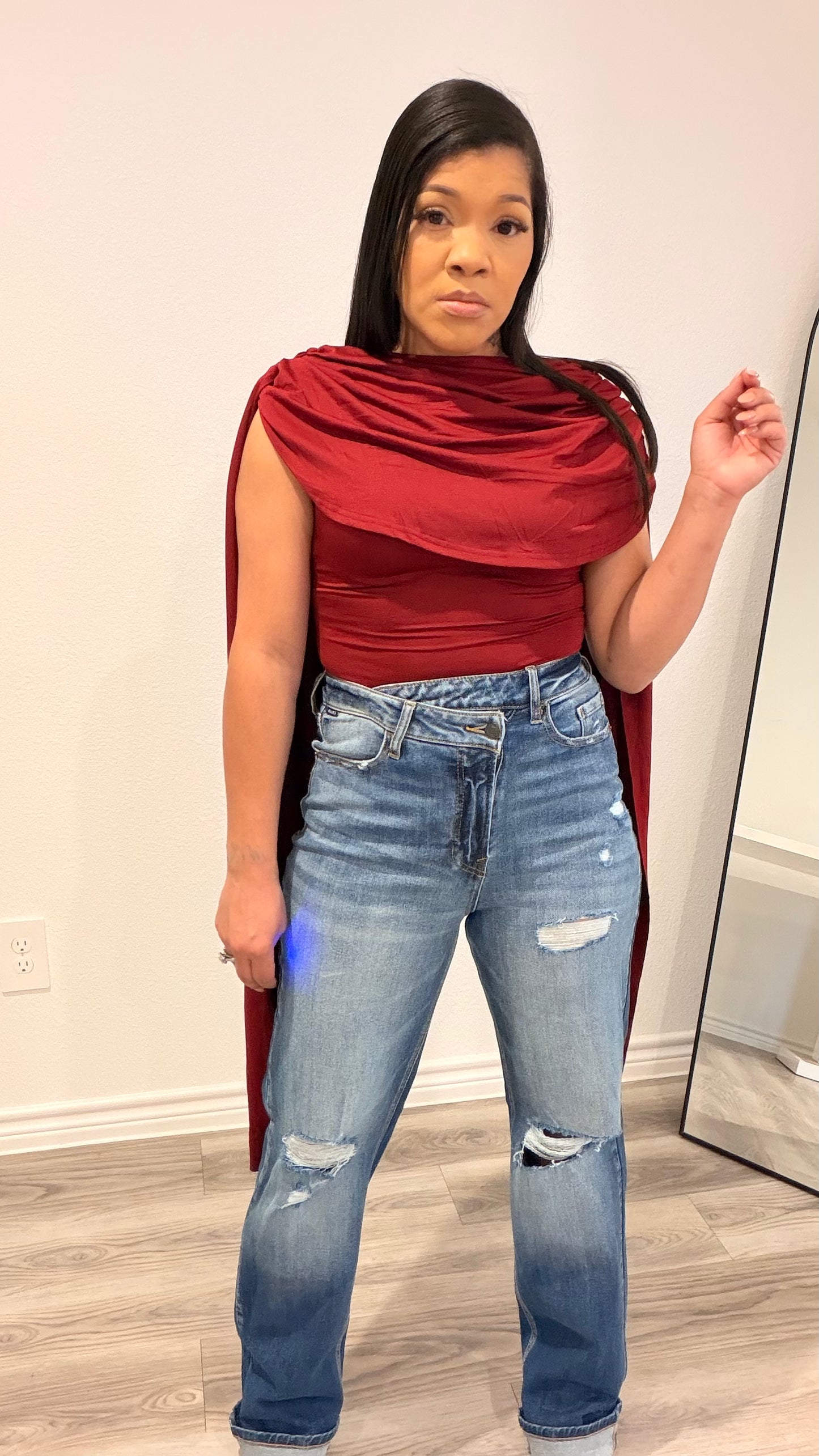 Woman wearing a bodysuit with cape-style draped sleeves and a fitted base.