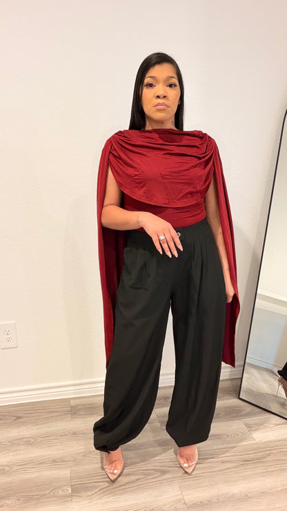 Woman wearing a bodysuit with cape-style draped sleeves and a fitted base.